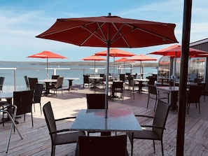 An outdoor patio with tables and chairs, red umbrellas, and a view of the water.