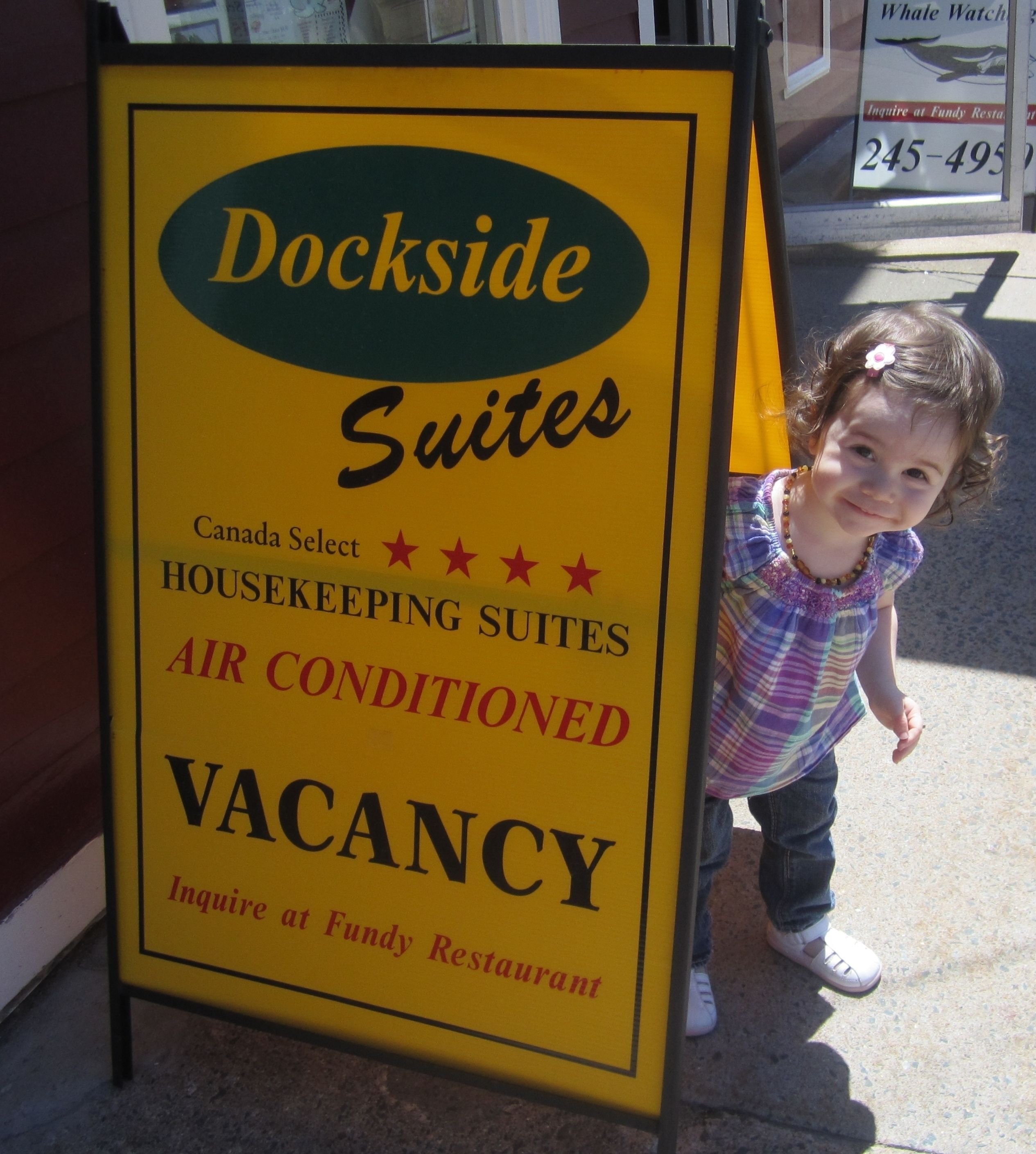 Un letrero amarillo anuncia Dockside Suites, limpieza Canadá Select, aire acondicionado y actualmente disponible.