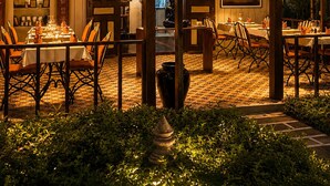 Un área de comedor al aire libre con mesas y sillas, una estructura de techo de paja y vistas a palmeras.