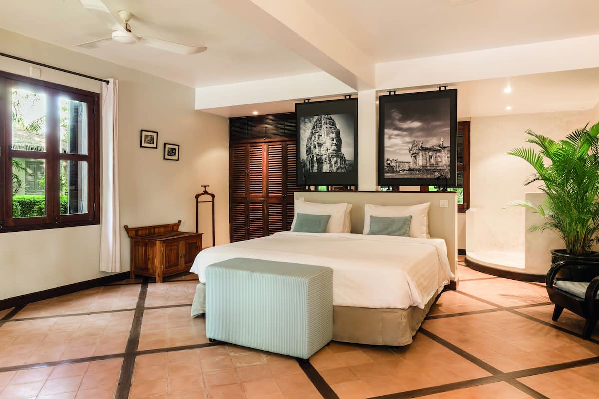 A bedroom with a bed, a nightstand, a potted plant, and artwork on the walls.