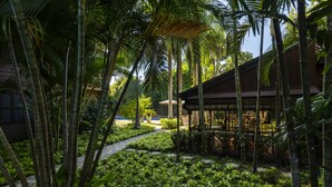 Camino en un jardín tropical que lleva a un edificio de madera con un espacio de estar al aire libre cubierto.