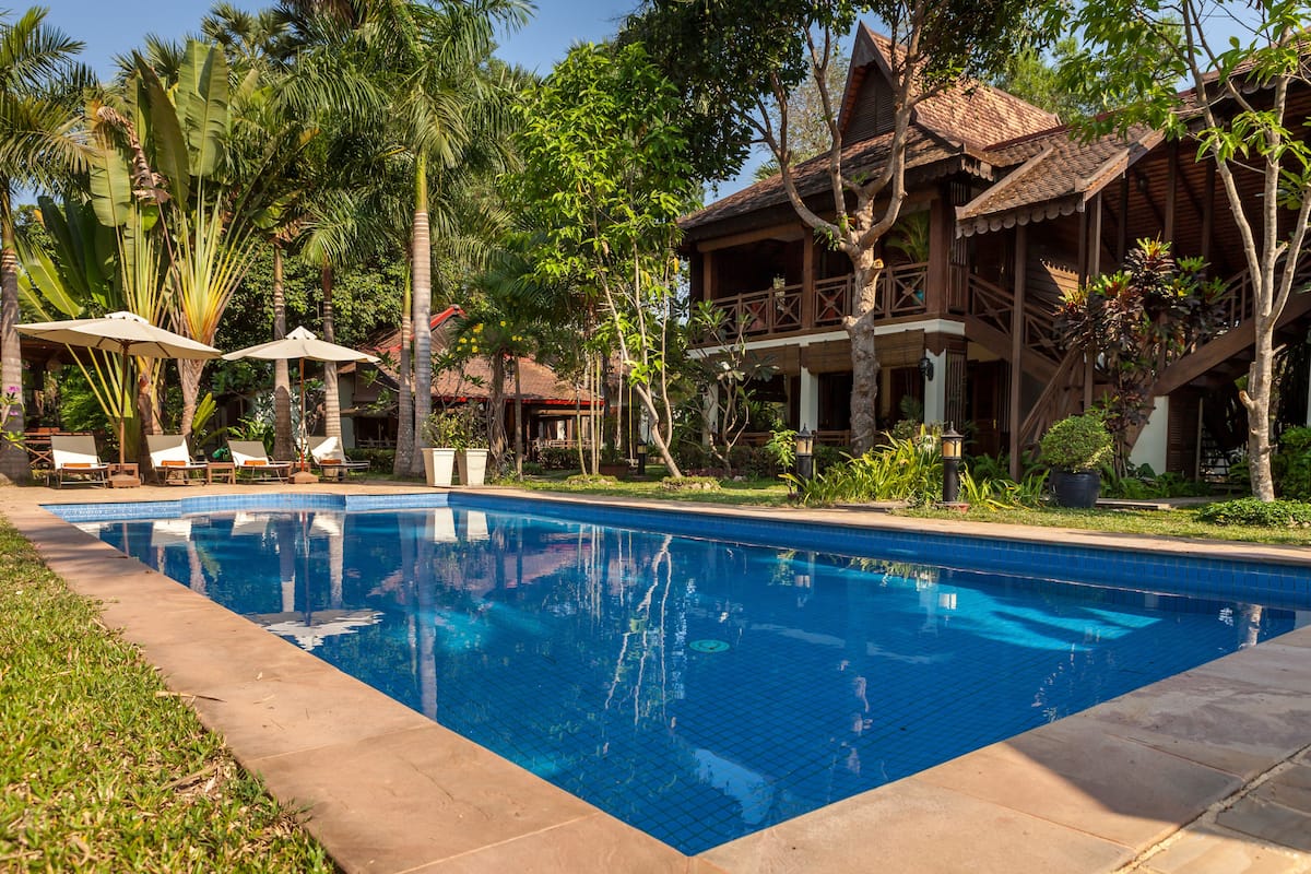 A swimming pool surrounded by lush greenery and a wooden building with a balcony.