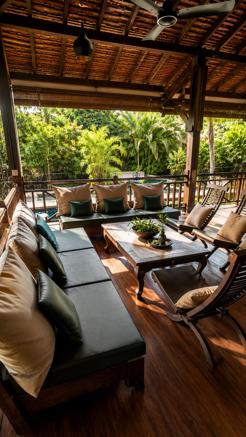 A covered outdoor seating area with wooden furniture, a ceiling fan, and a view of lush greenery.