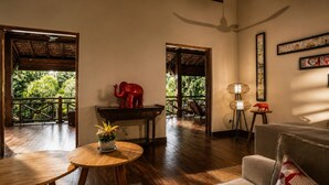 Una habitación con piso de madera, una mesa redonda con un jarrón, un sofá, una escultura de elefante rojo y un ventilador de techo.