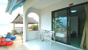 Un balcon avec une table et des chaises, une porte vitrée et une vue sur la plage et les bateaux.