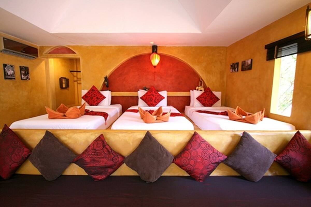 Ein Hotelzimmer mit drei Betten, jedes mit roten und braunen Kissen, und einem großen Bogenfenster.