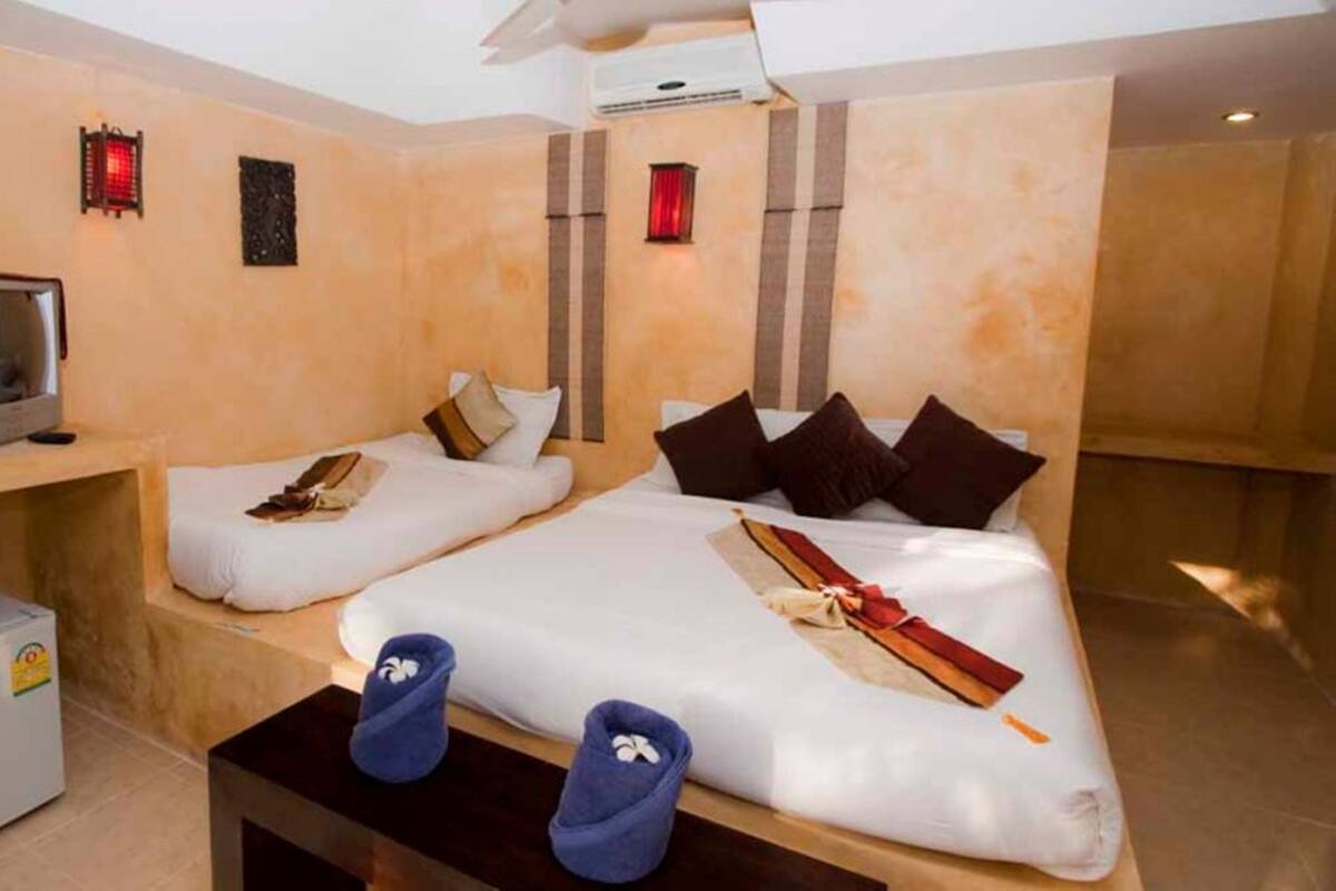 Ein Hotelzimmer mit zwei Einzelbetten, einem Fernseher, einer kleinen Minibar und Hausschuhen auf dem Bett.