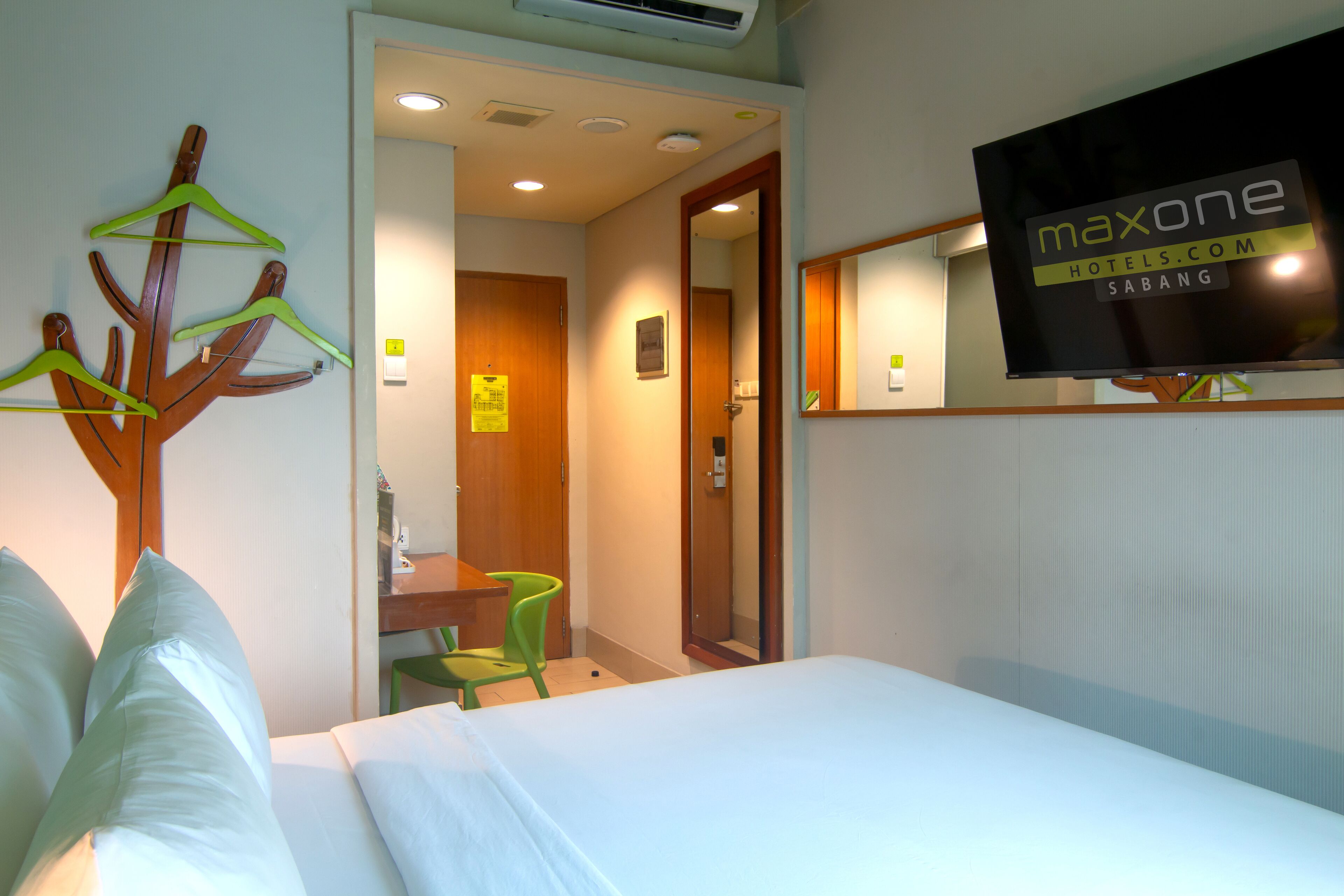Camera d'albergo con un letto, una scrivania, una sedia e una TV a parete che mostra il nome dell'hotel.