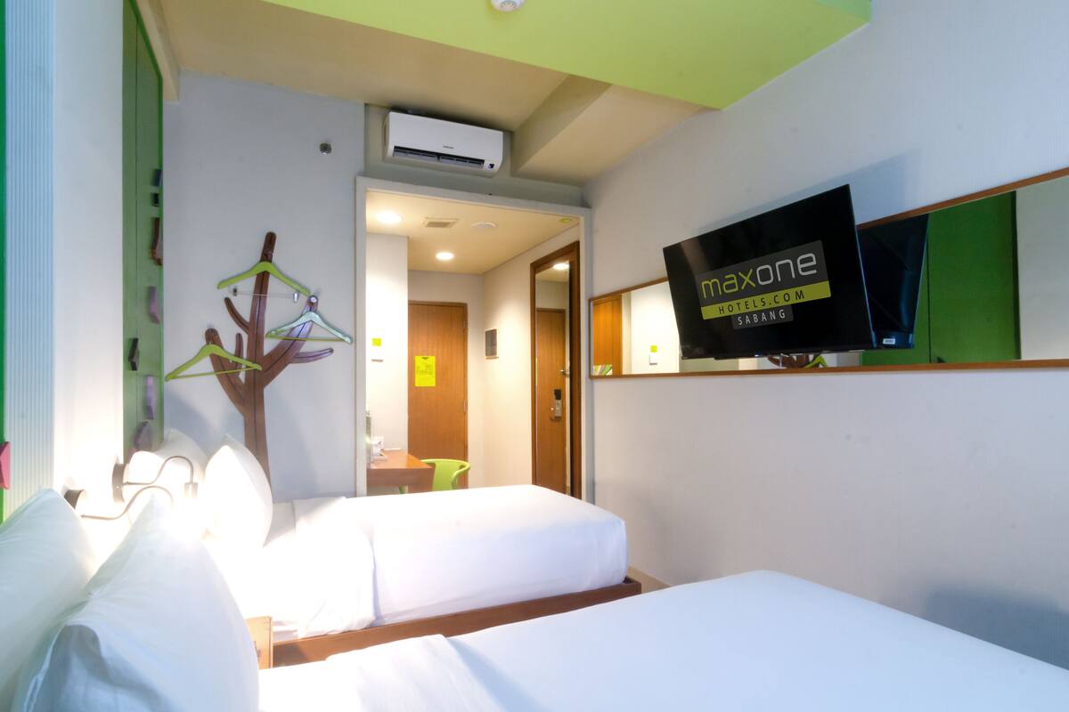 A hotel room with two beds, a TV mounted on the wall, and an air conditioning unit above the beds.