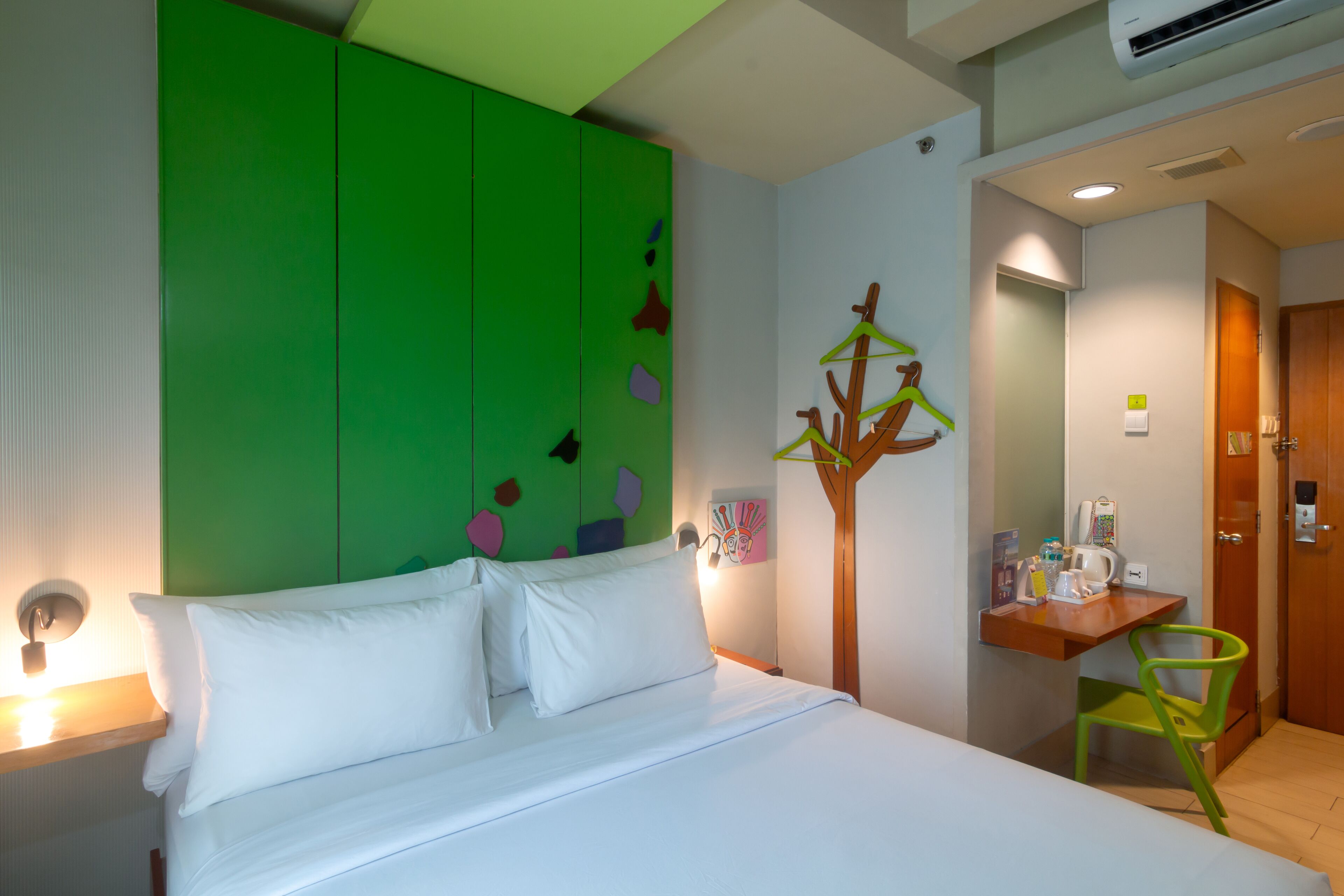 A hotel room with a bed, a desk, a chair, and a wall-mounted coat rack.