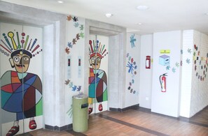 A hallway with colorful murals, a fire extinguisher, and a trash bin.