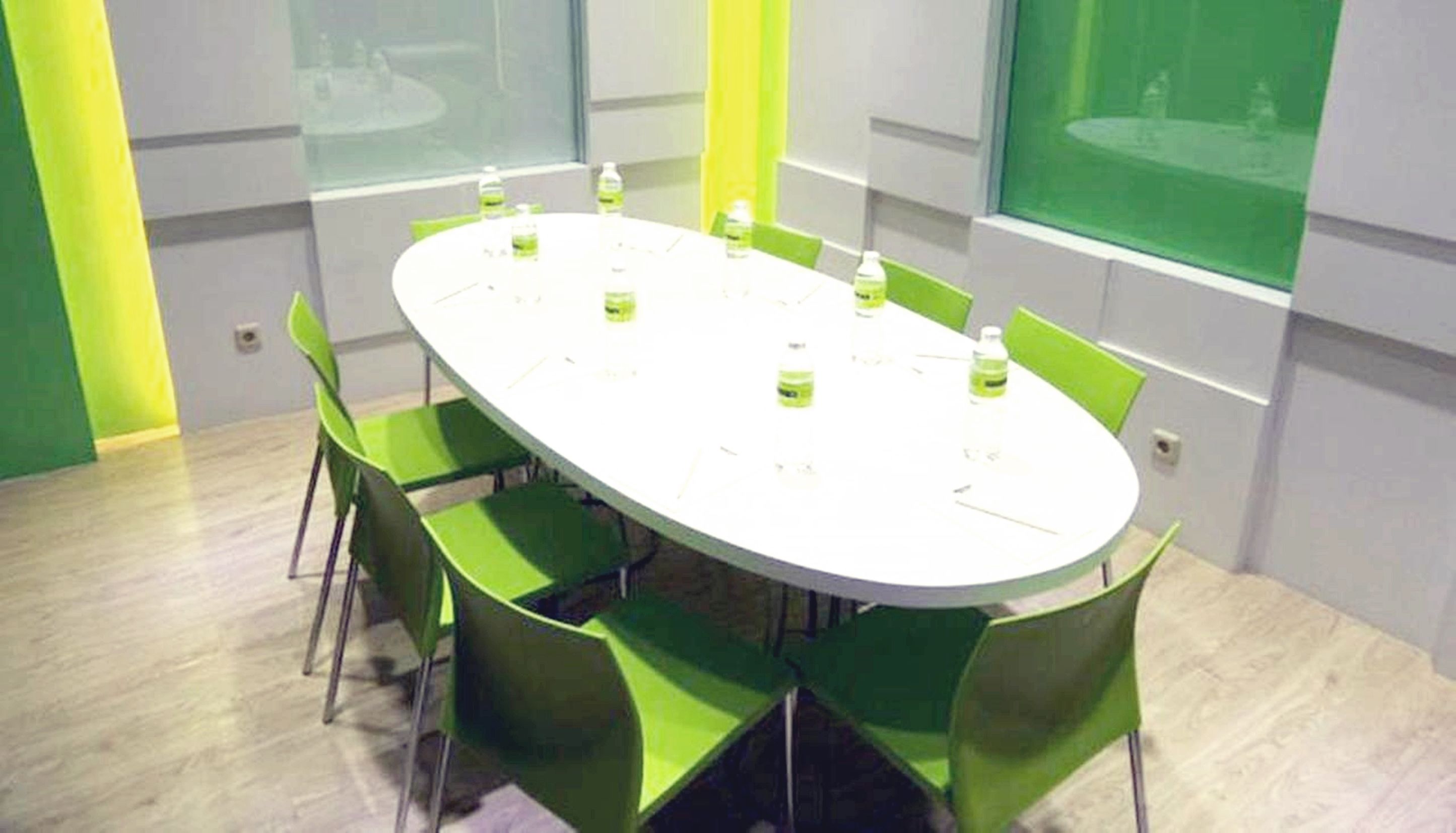 A conference room with a white oval table, green chairs, and water bottles on the table.