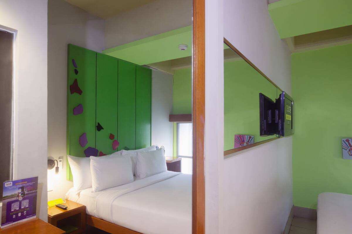 A hotel room with a bed, a nightstand, a green wardrobe, a mirror, and a TV.