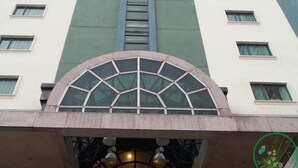 Un hotel alto con una entrada central que cuenta con un toldo de vidrio y un logotipo circular sobre la entrada.