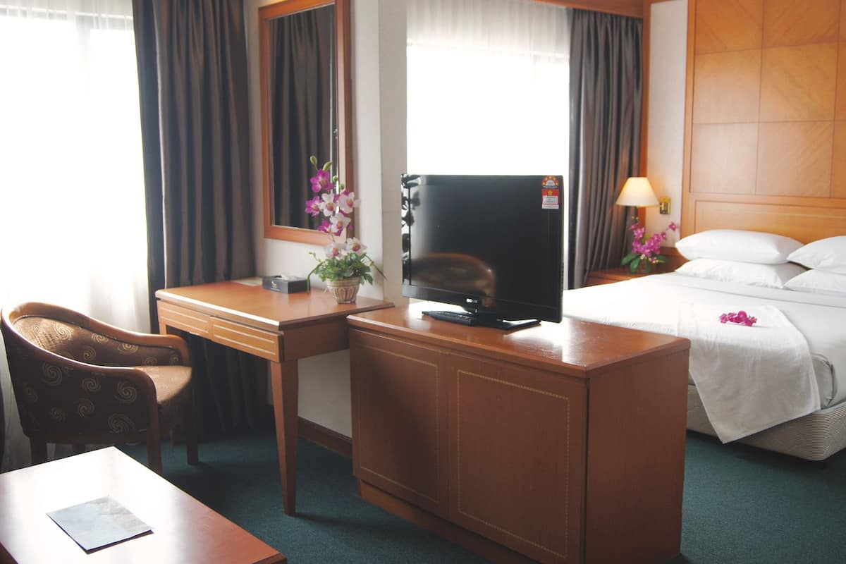 Quarto de hotel com cama, escrivaninha com televisão, cadeira e uma mesinha.