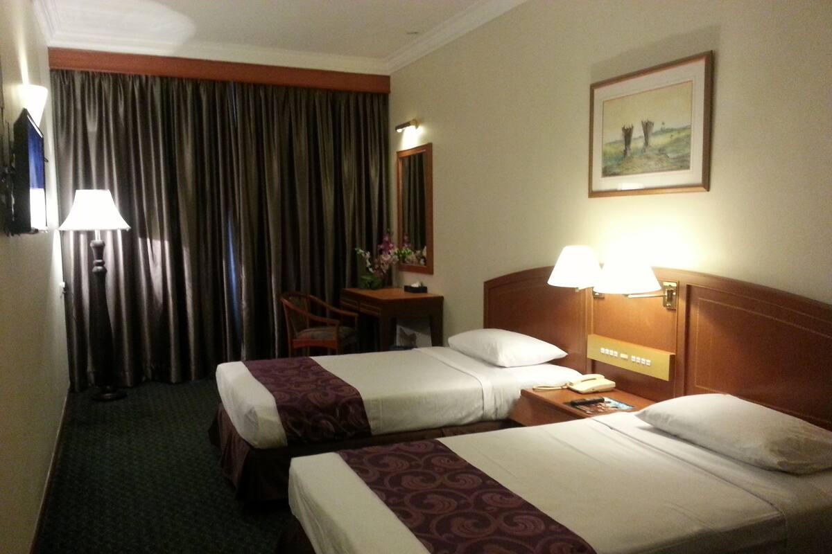 Quarto de hotel com duas camas, uma escrivaninha, uma cadeira, um abajur e um quadro na parede.