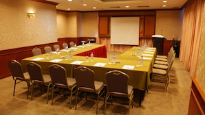 Un salón de conferencias con una larga mesa, sillas, botellas de agua y una pantalla para proyector.