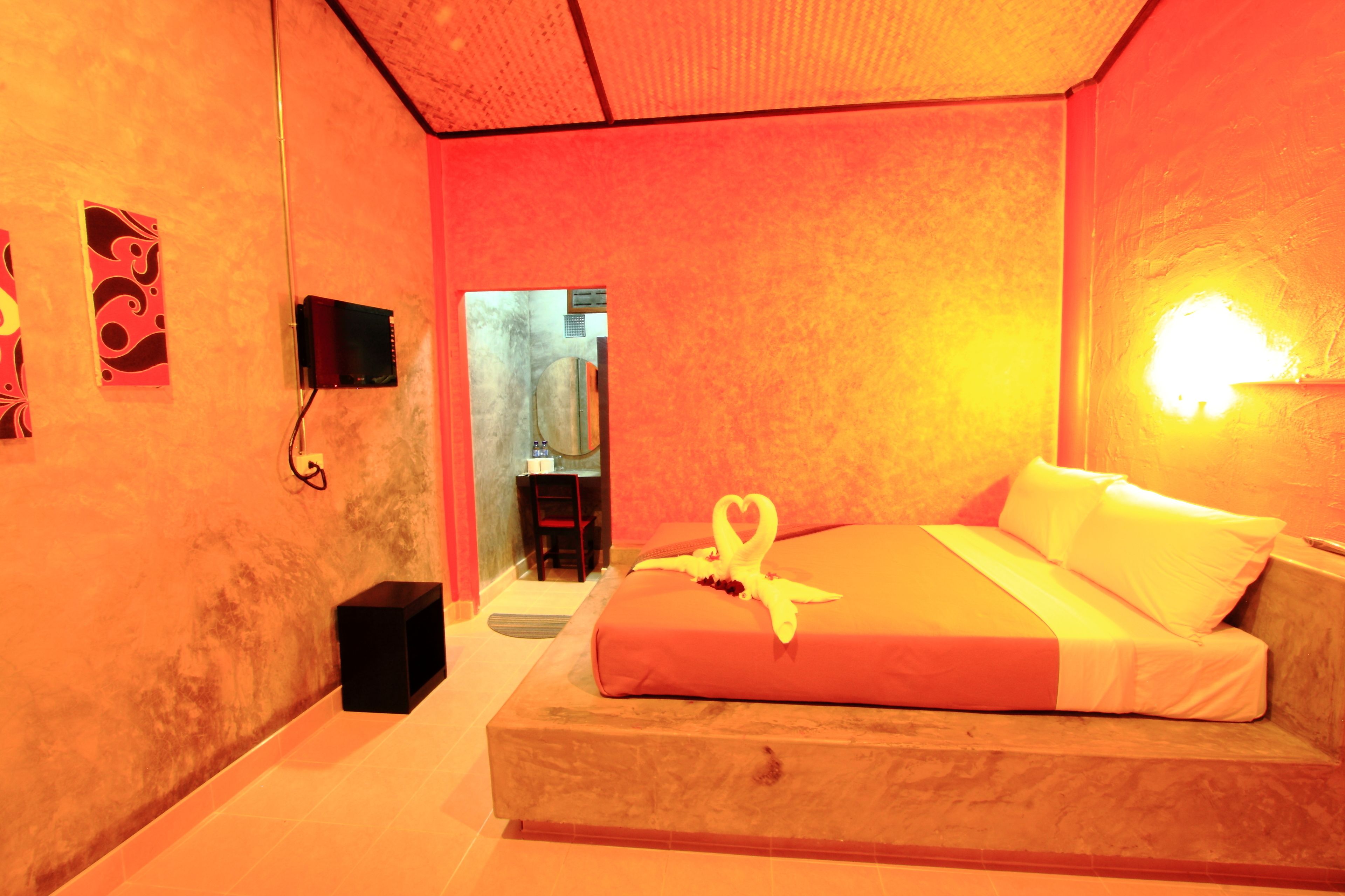 A hotel room with a bed, a bedside table, a wall-mounted TV, and a door leading to a bathroom.
