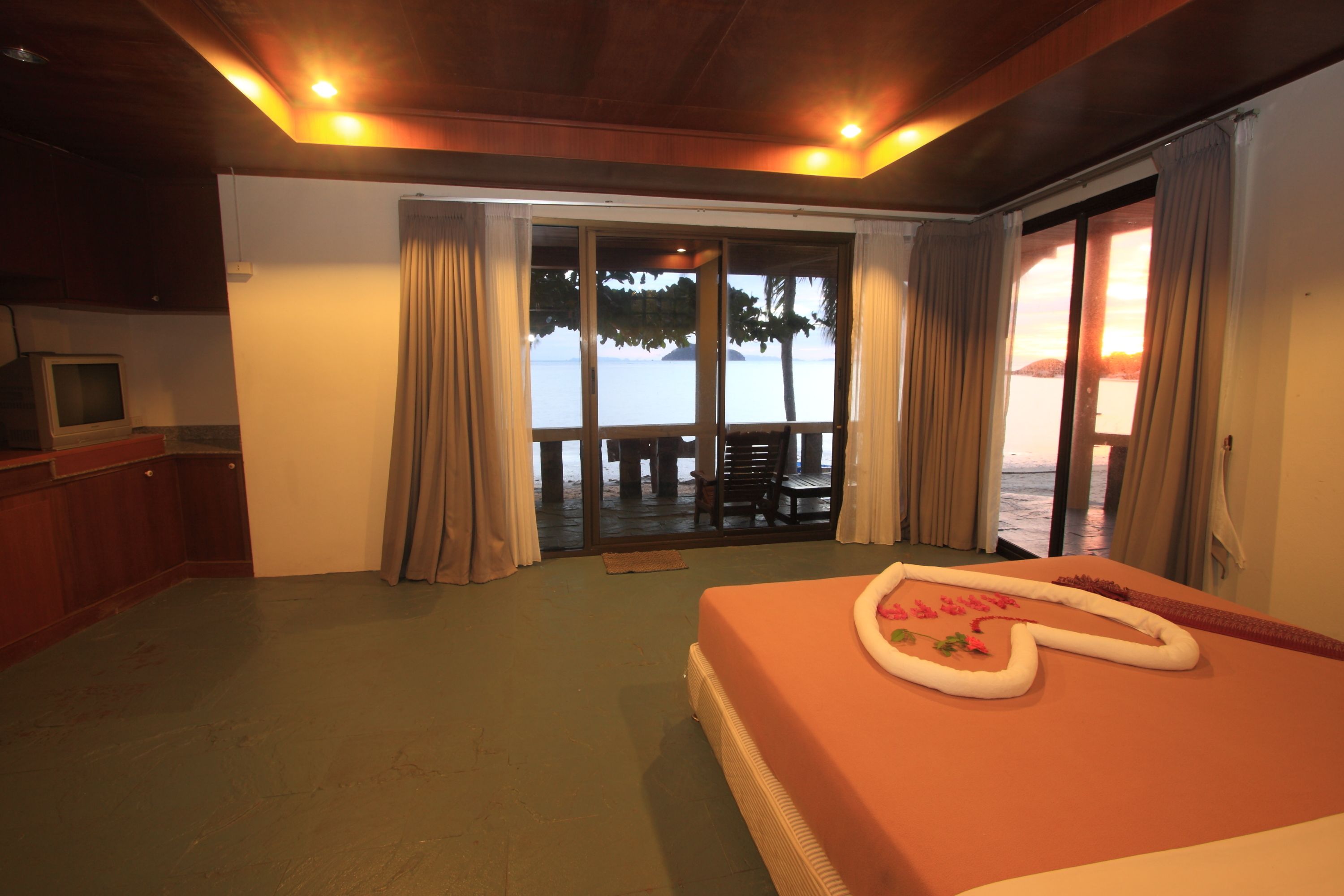 Quarto de hotel com cama, televisão e vista para o mar através de uma porta de correr de vidro.