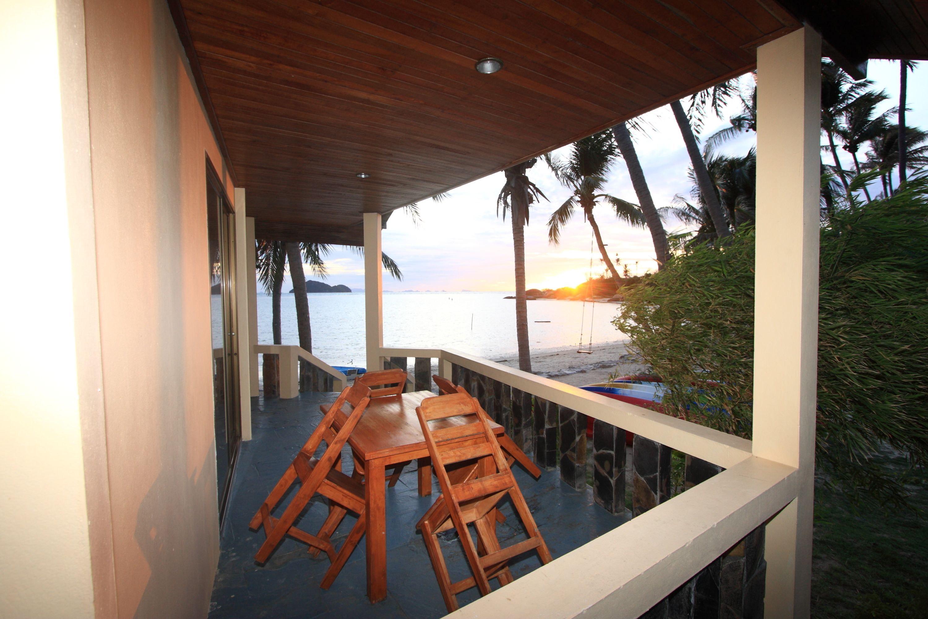 A covered outdoor seating area with a view of the beach and ocean at sunset.