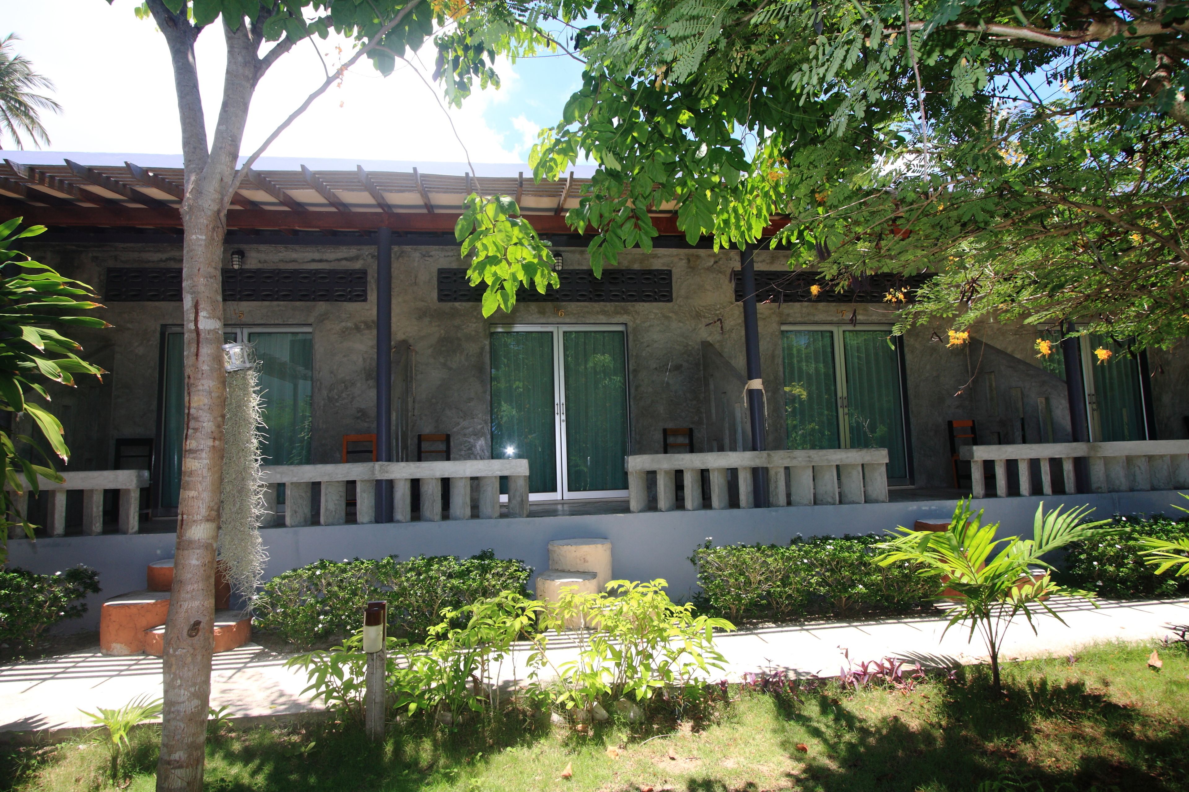 A building with a modern architectural style, featuring a flat roof and large windows. There is a well-maintained garden with various plants and a pathway leading to the entrance.
