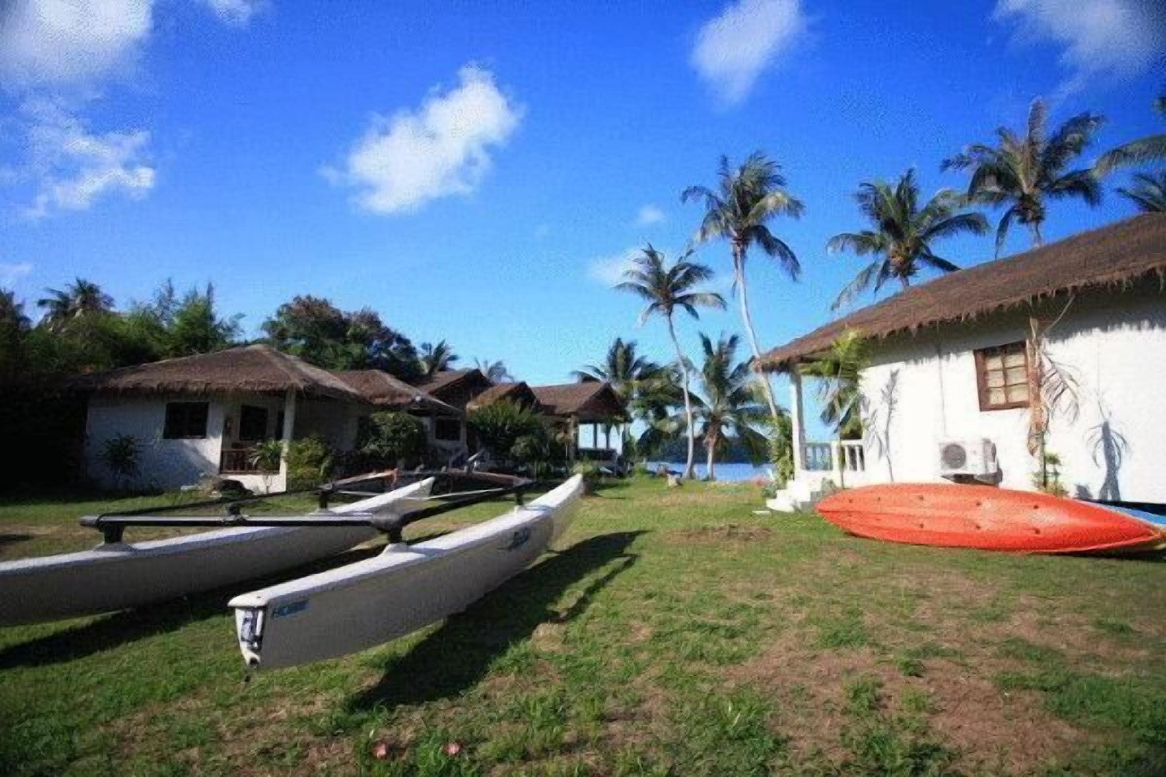 A beachside property with thatched-roof cottages, a grassy lawn, and a row of canoes.