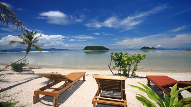 A beach with two wooden lounge chairs and a small table, a palm tree, and a view of the sea with islands in the distance. - Beck 's Resort (Ko Pha-ngan)