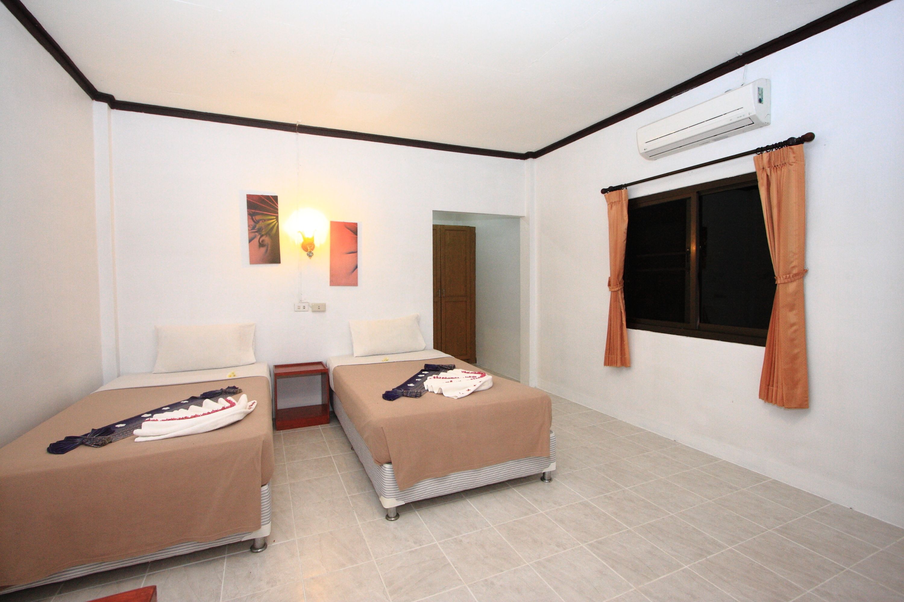 A hotel room with two single beds, a nightstand, a wall-mounted air conditioner, and a window with curtains.