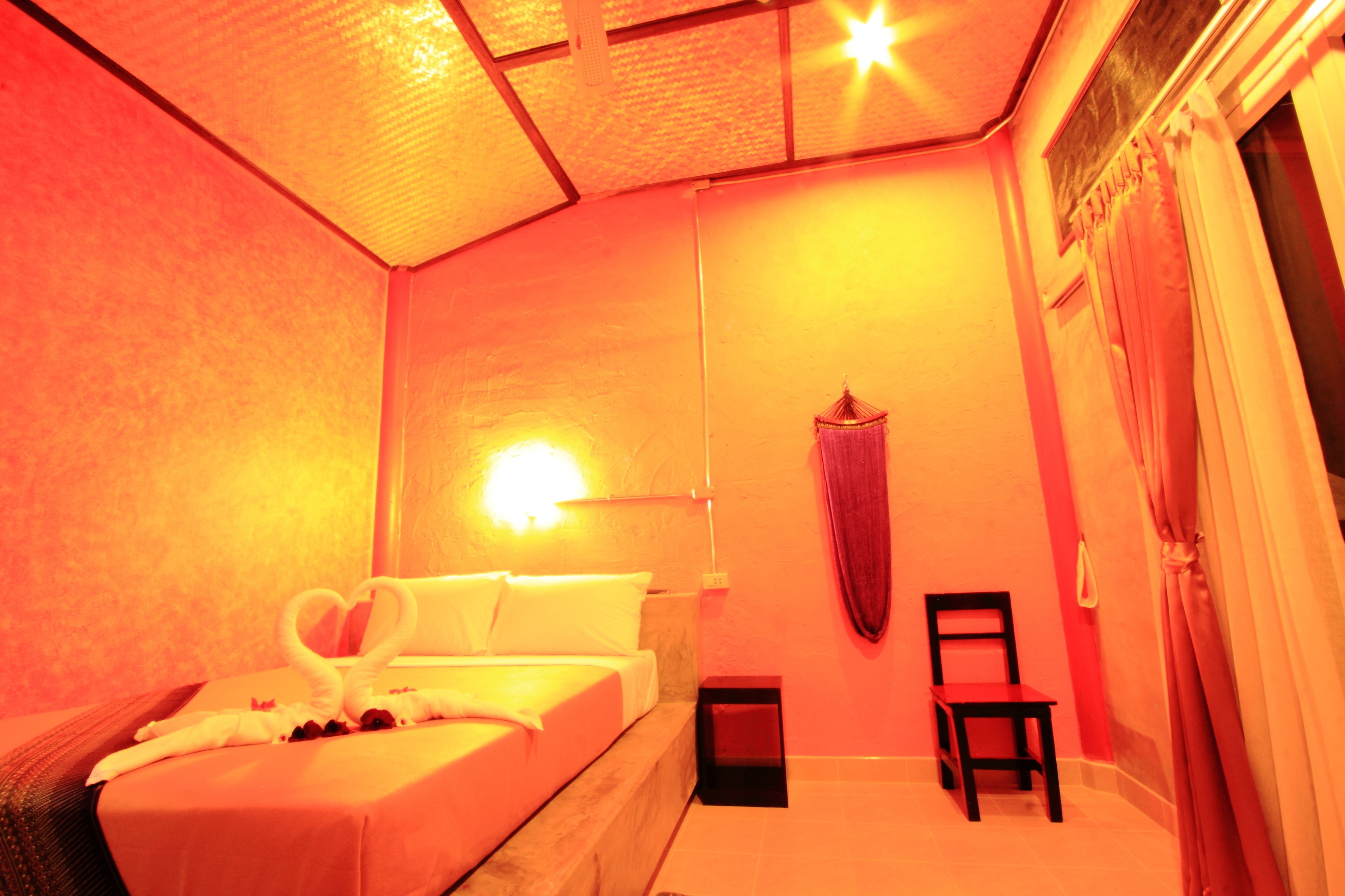Una habitación con una cama, una silla, una lámpara de pared y una cortina.