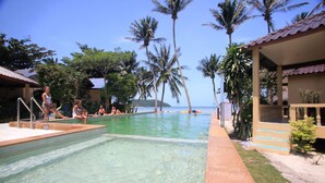 A pool area with clear water, surrounded by palm trees and a building with a tiled roof. - Beck 's Resort (Ko Pha-ngan)