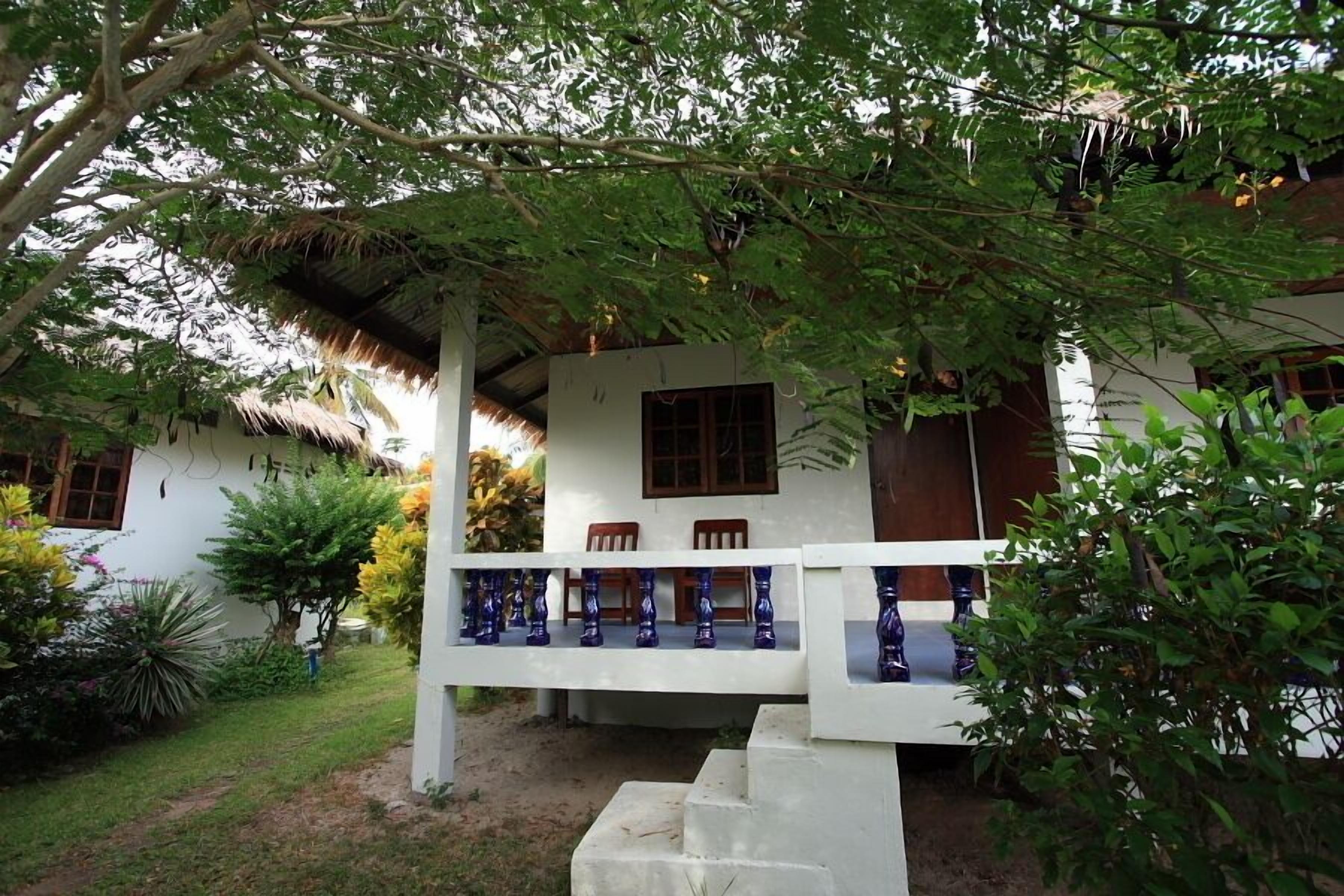 A white building with a thatched roof, a balcony with blue balustrades, and a small staircase leading to the entrance.