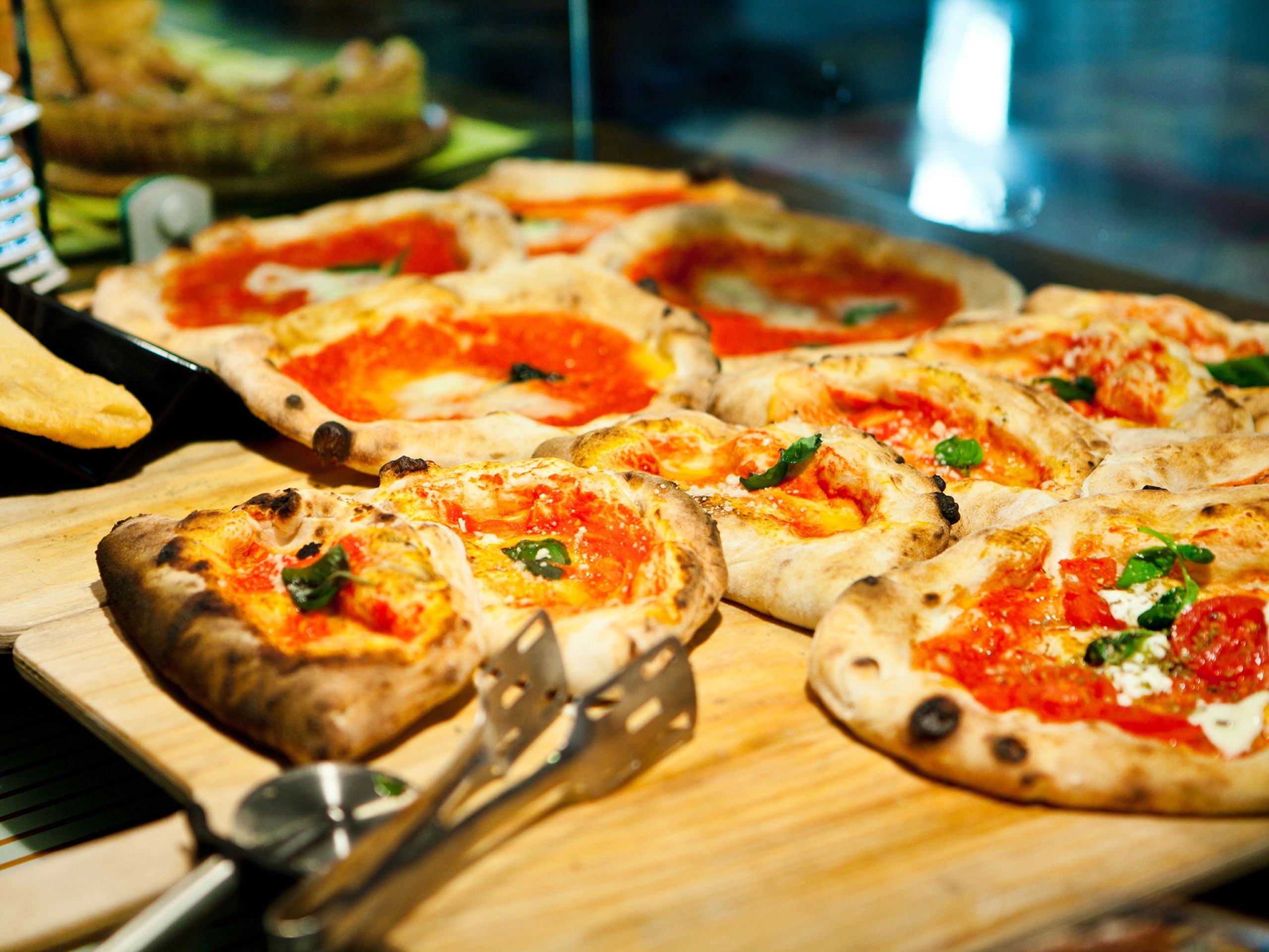 A wooden cutting board with several pizzas topped with cheese and herbs.