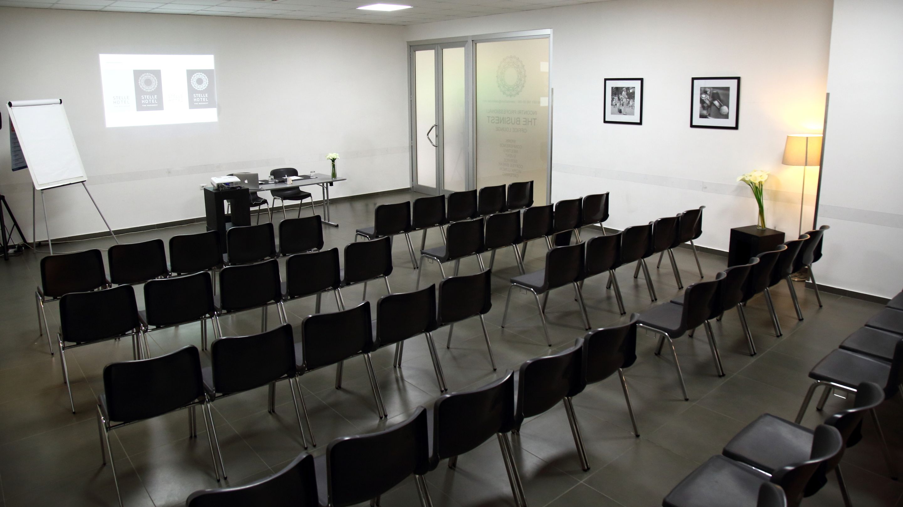 A conference room with rows of black chairs, a whiteboard, and a projector screen.