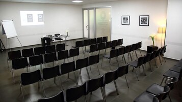 Una sala conferenze con file di sedie nere, una lavagna e uno schermo per proiettore.