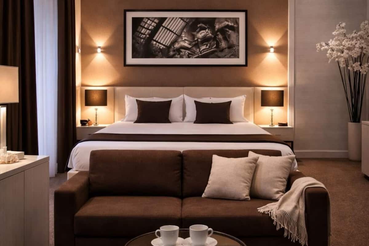 A hotel room with a bed, a sofa, a coffee table, and a framed artwork on the wall.