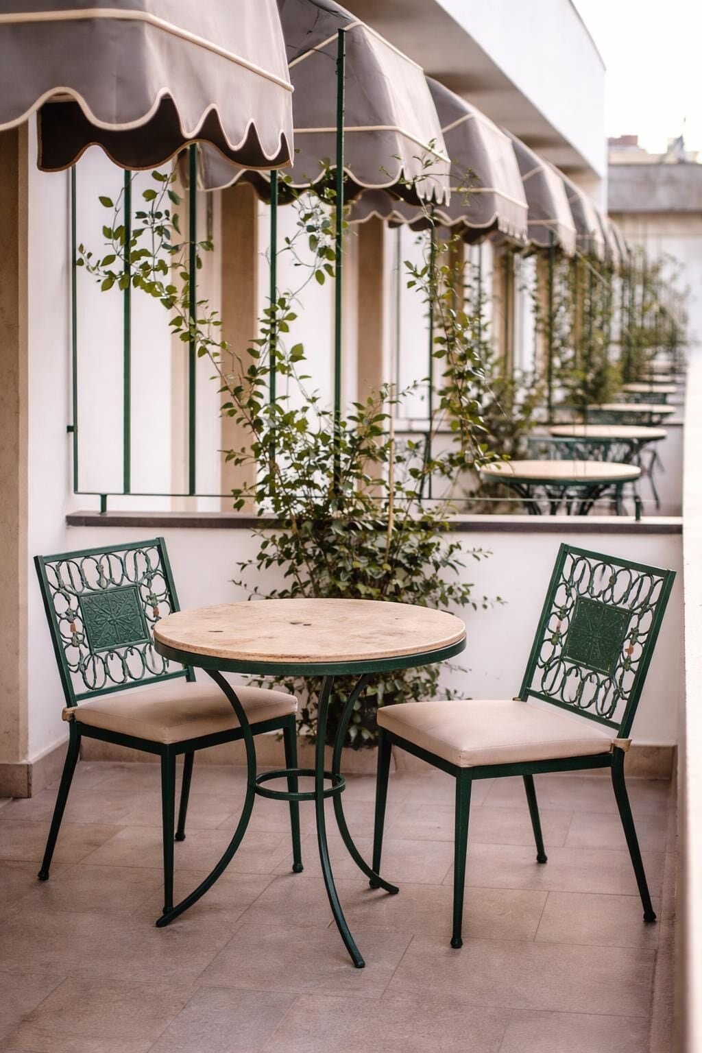 A patio with two chairs and a table, surrounded by a row of windows with plants.