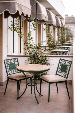 A patio with two chairs and a table, surrounded by a row of windows with plants. - Stelle Hotel The Businest (Naples)