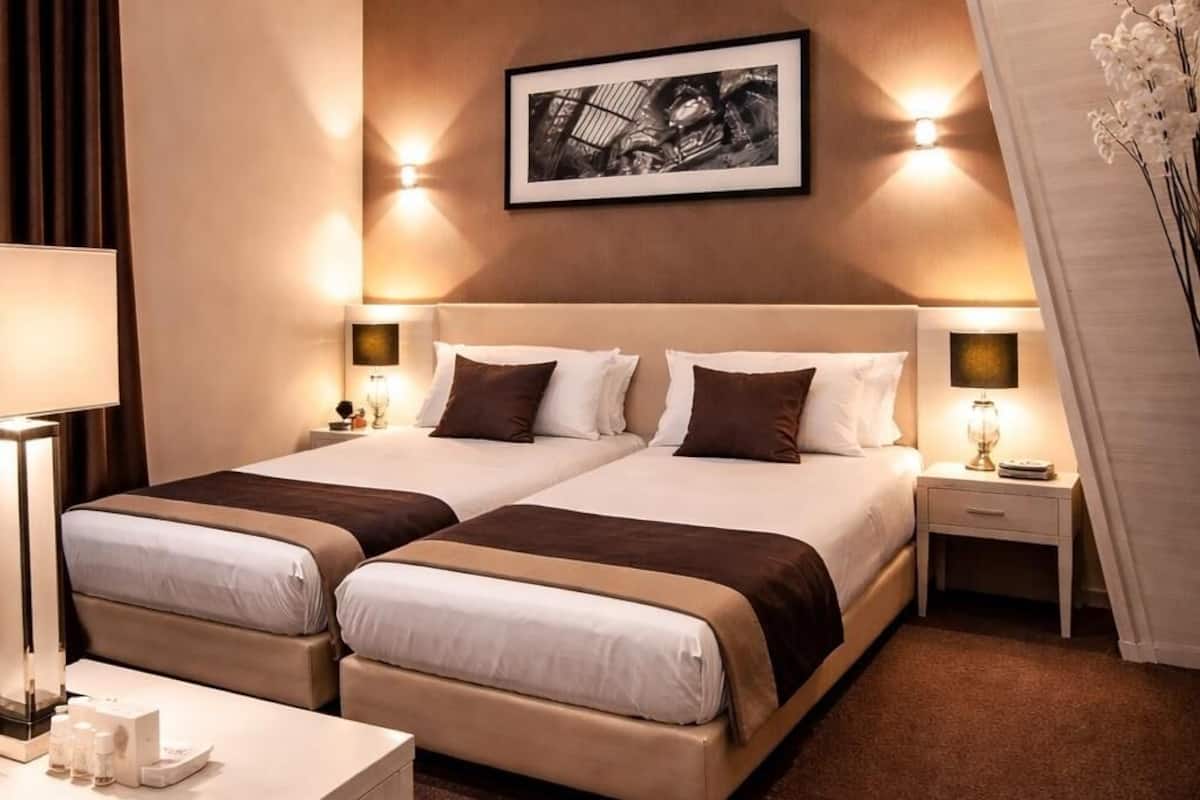 A hotel room with a large bed, two bedside tables, a desk, and a framed picture on the wall.