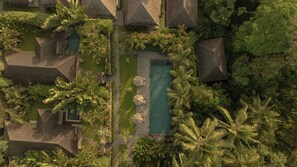 An aerial view of a resort with thatched-roof buildings, a swimming pool, and lush tropical vegetation. - Suara Air Resort Ubud (Ubud)