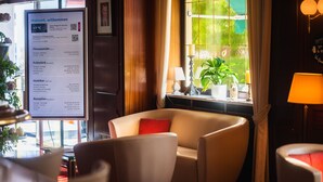 Un hall d’hôtel doté d’une grande fenêtre, d’un comptoir d’accueil et d’un espace détente avec un coussin rouge.