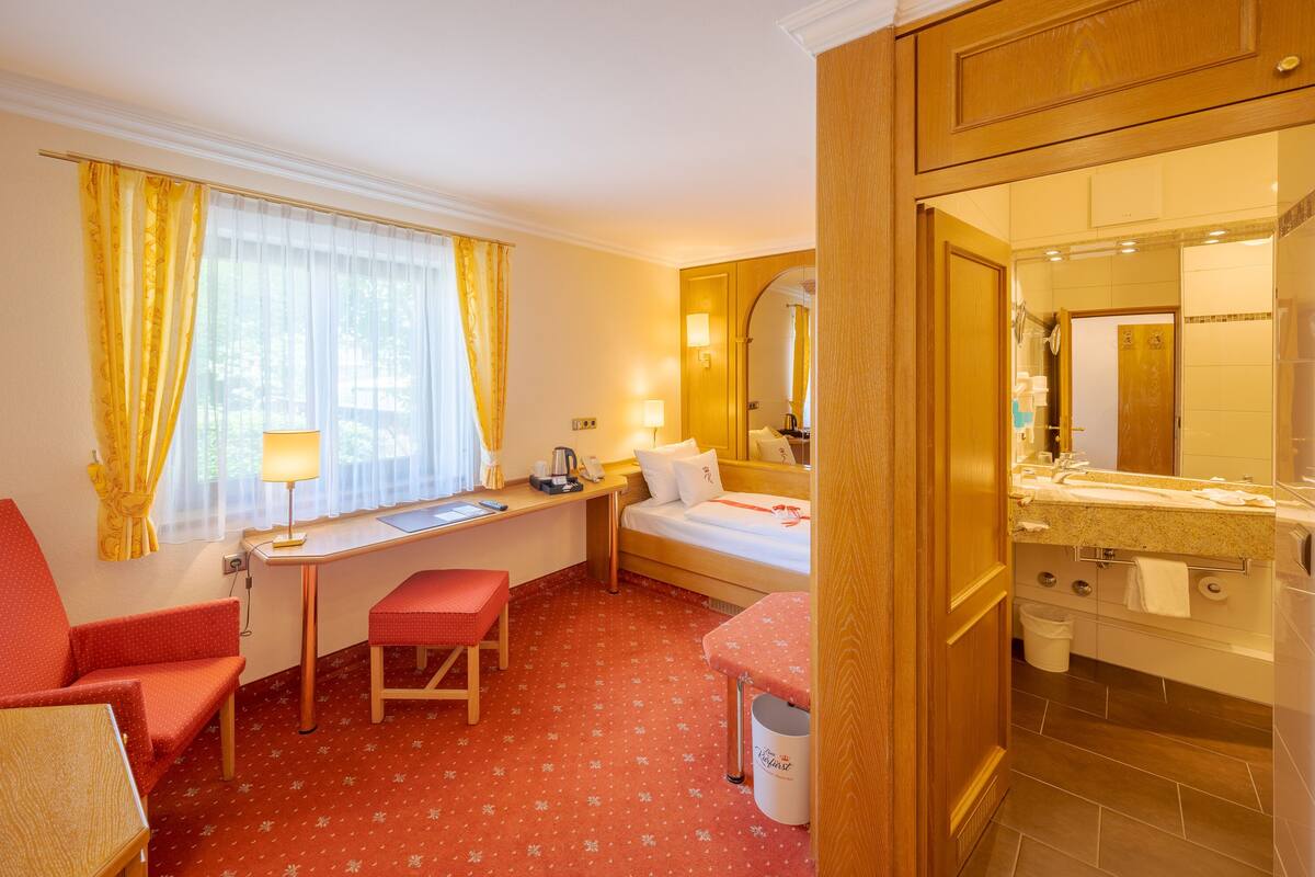 Une chambre d’hôtel comprenant un lit, un bureau, une chaise et une salle de bain avec un lavabo et un miroir.