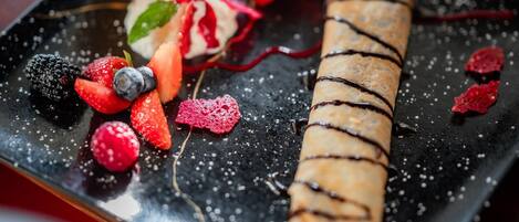 Un plato de postre con un pastel enrollado, fresas, frambuesas y un chorrito de salsa.