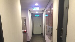 A hallway with a carpeted floor, a door at the end, and a sign above indicating an exit. - Royal Hotel (Taipei)