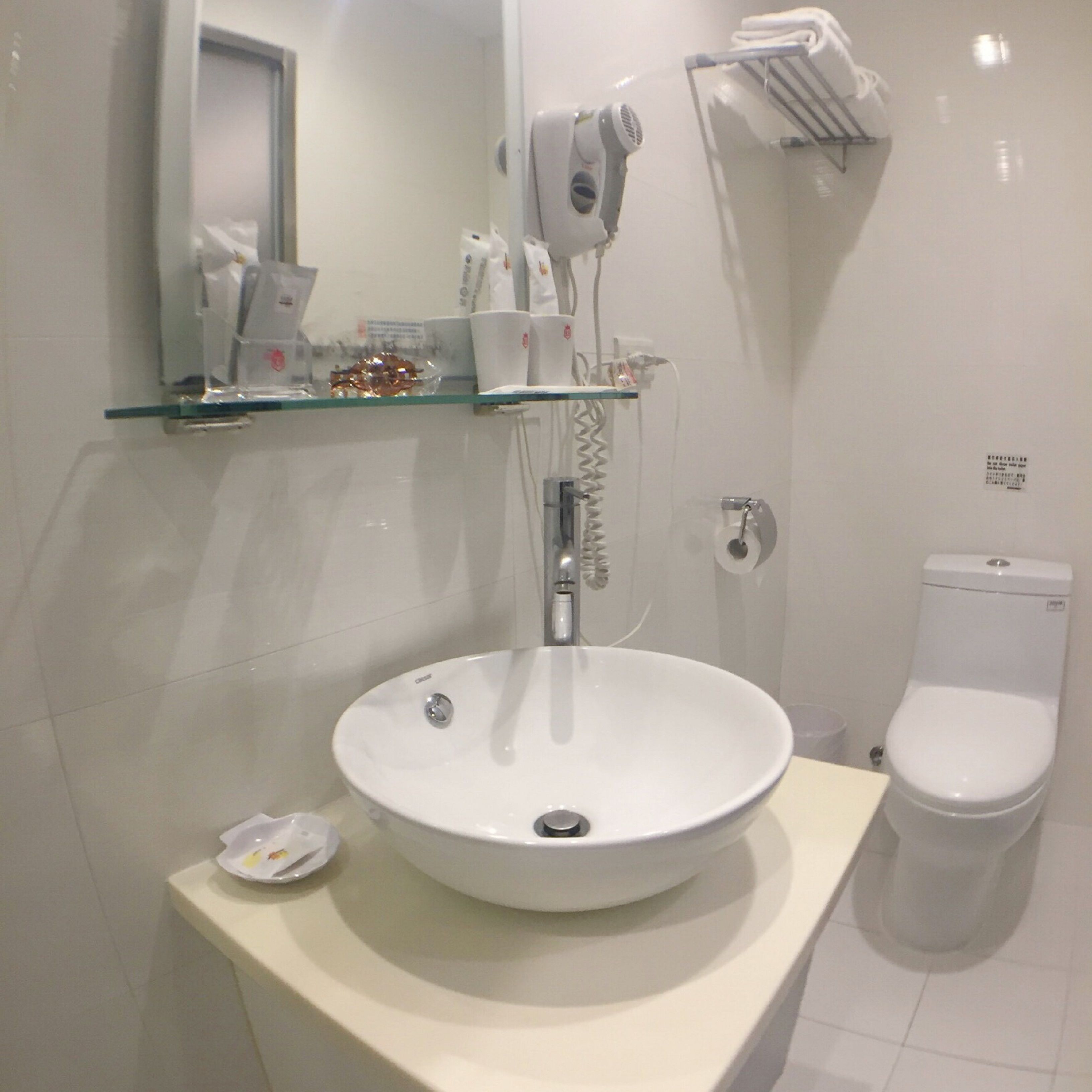 A bathroom with a white sink, a toilet, and a glass shelf above the sink.