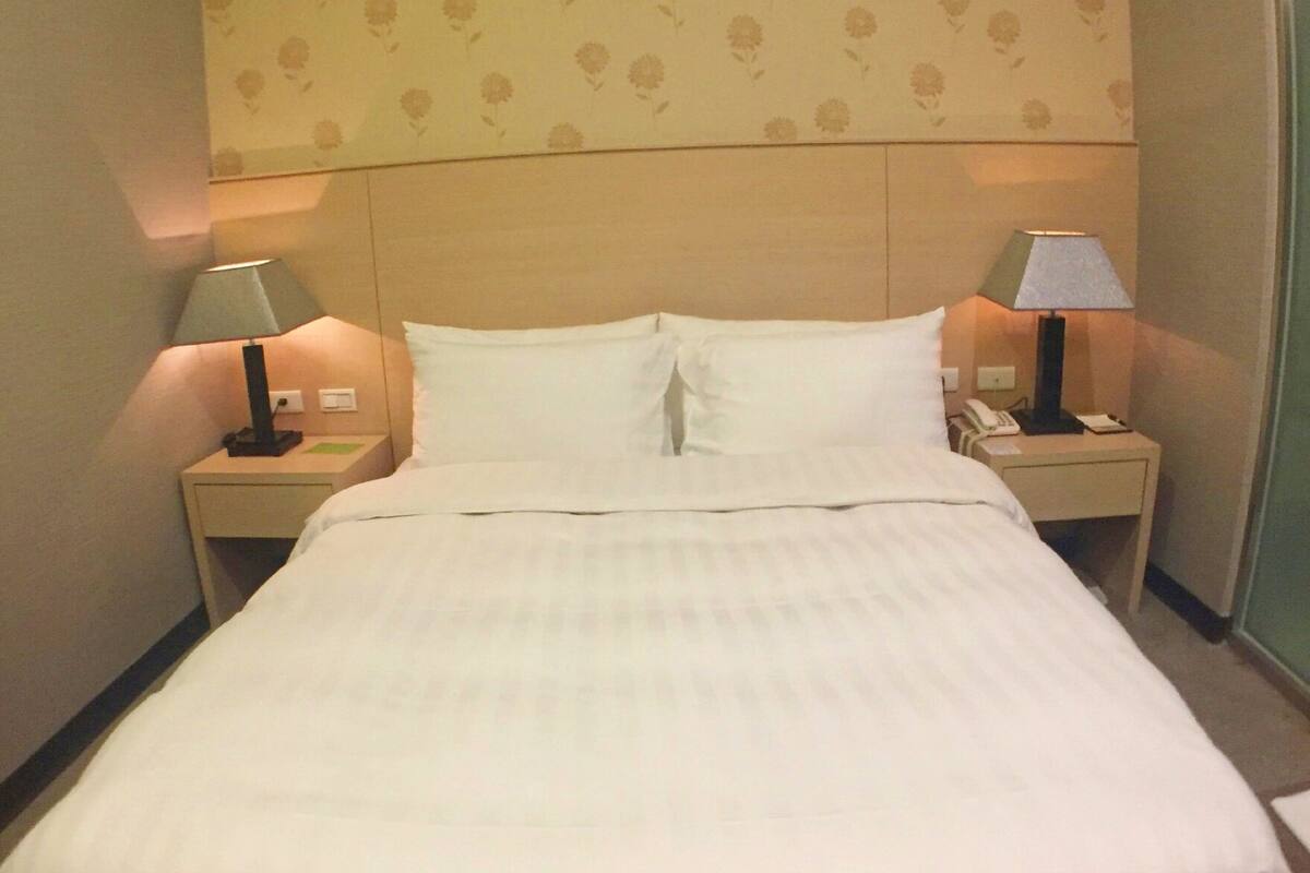A neatly made bed with white linens in a hotel room.