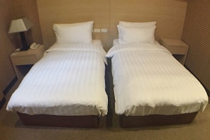 A hotel room with two single beds, a nightstand with a lamp, and a small table with a phone.