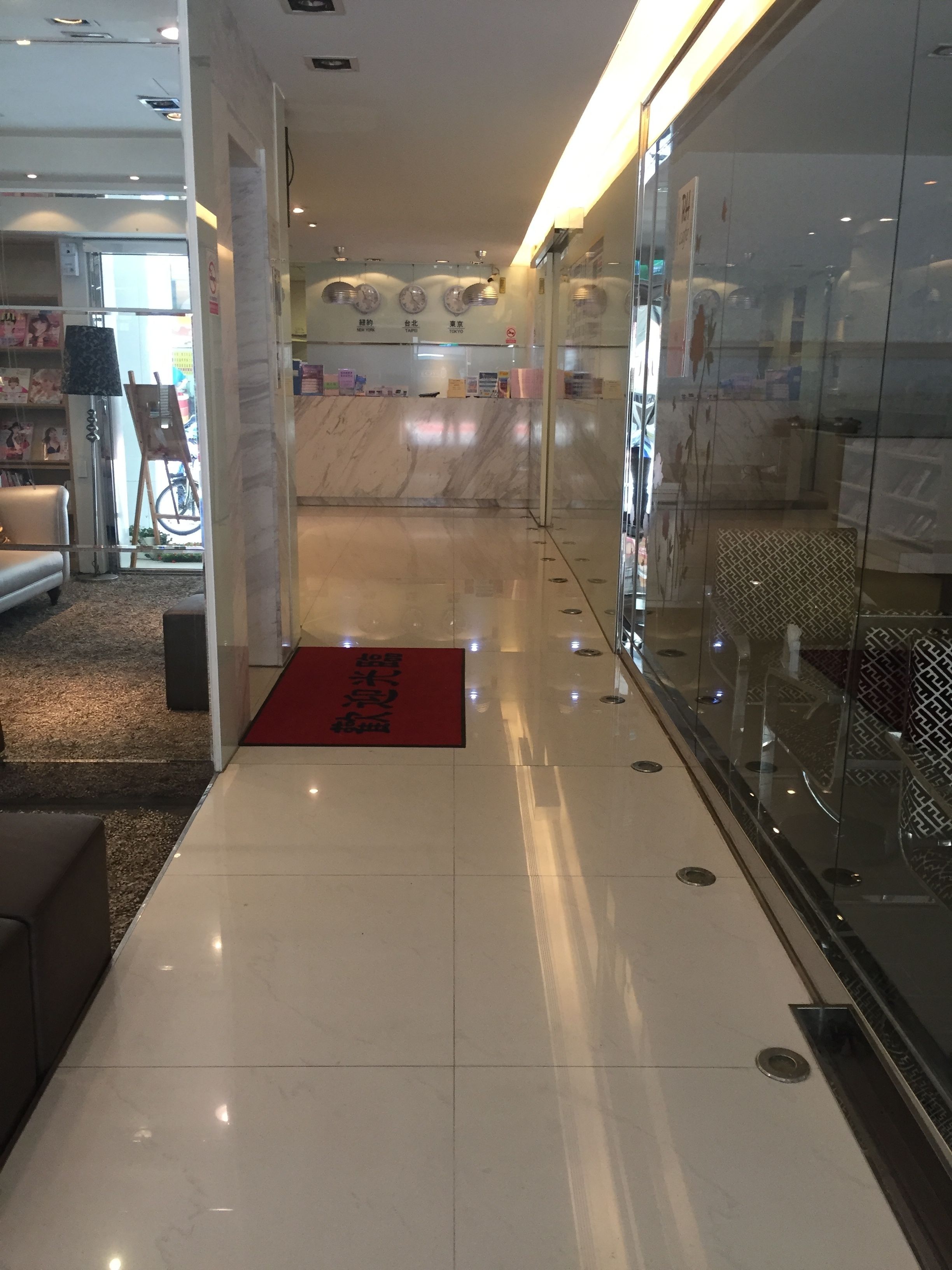 A hallway with a red mat, a glass wall, and a marble floor.