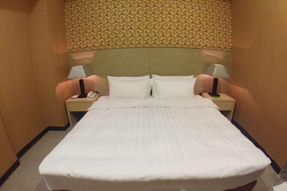 A hotel room with a large bed, two bedside tables, and a headboard with a floral pattern.