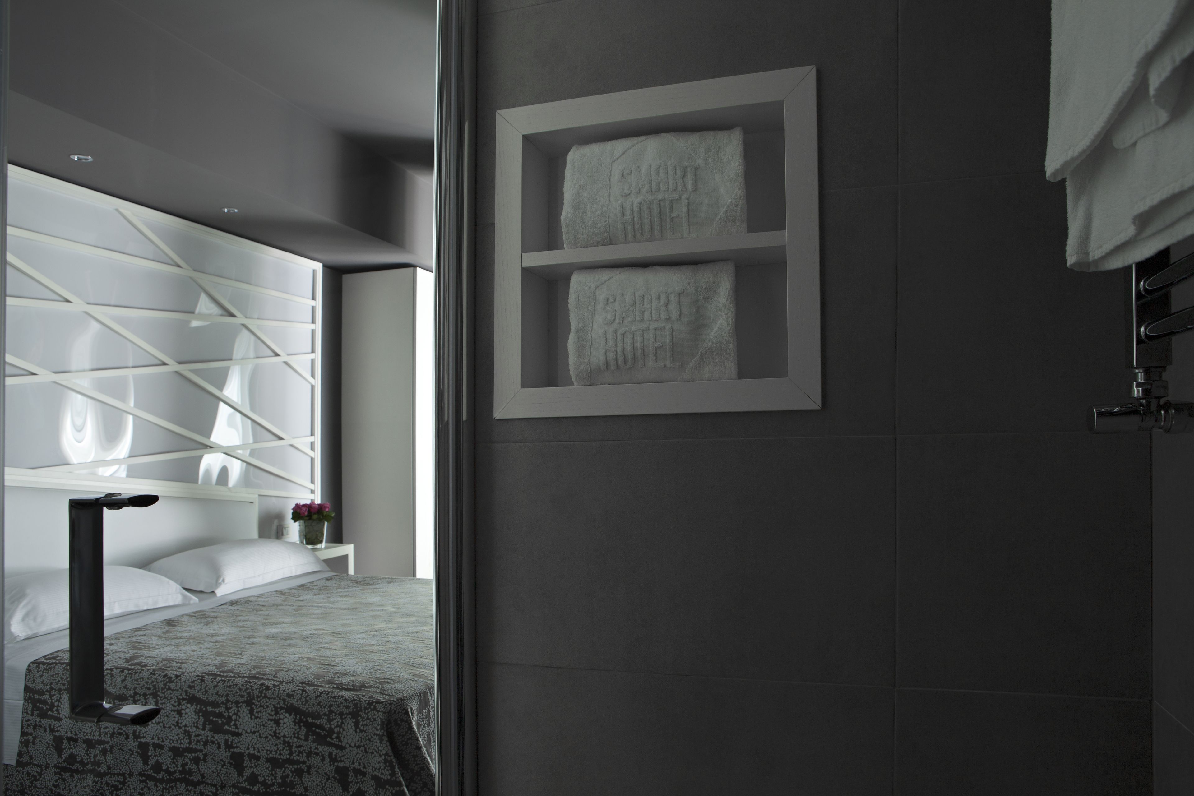 A modern hotel room with a bed, a nightstand, and a wall-mounted towel rack.