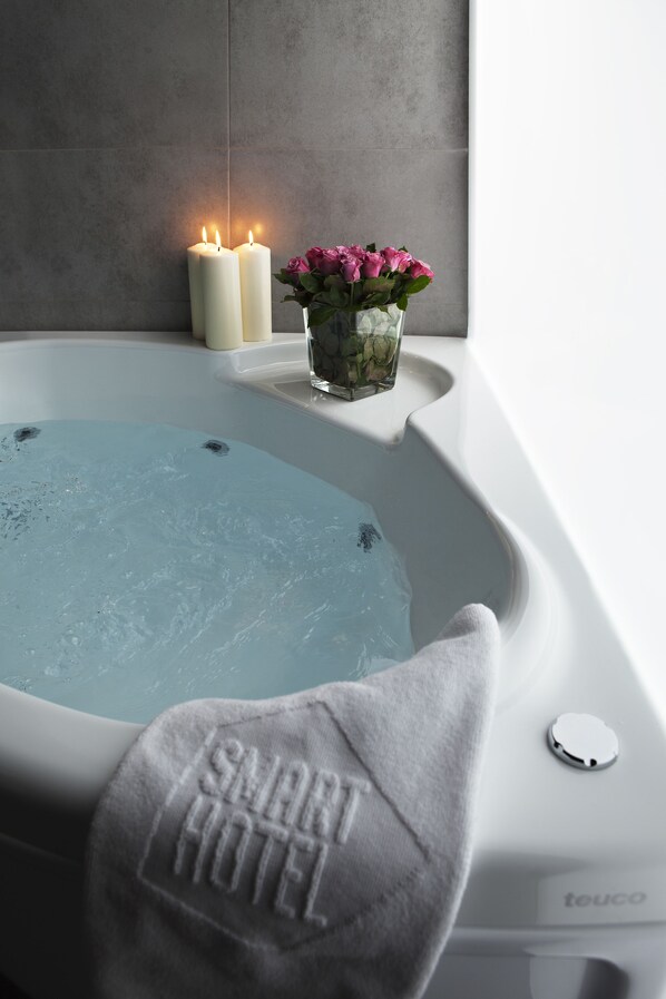 A bathtub with two lit candles and a vase of pink flowers.